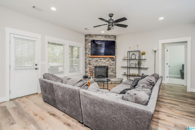 living room with a stone fireplace, light wood-type flooring, and ceiling fan