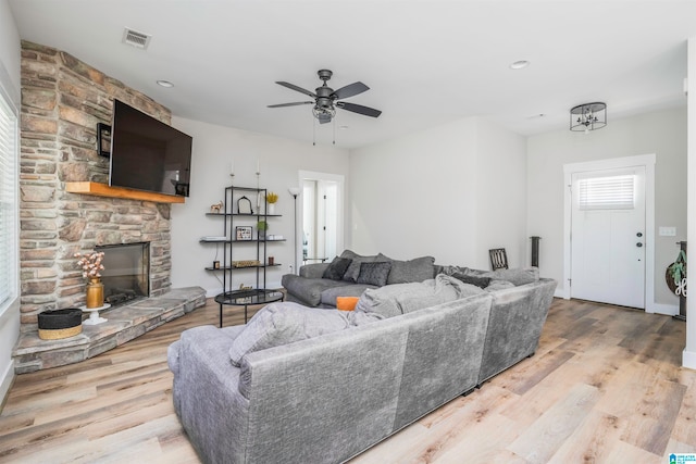 living room featuring ceiling fan, a stone fireplace, and light wood-type flooring