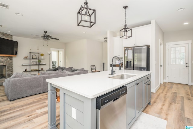 kitchen featuring a stone fireplace, an island with sink, white cabinets, light wood-type flooring, and appliances with stainless steel finishes