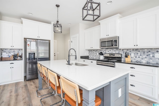 kitchen with appliances with stainless steel finishes, a kitchen island with sink, sink, and pendant lighting