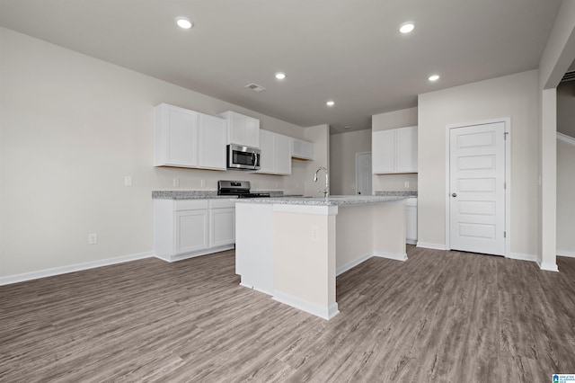 kitchen featuring light stone countertops, white cabinetry, stainless steel appliances, an island with sink, and light hardwood / wood-style floors