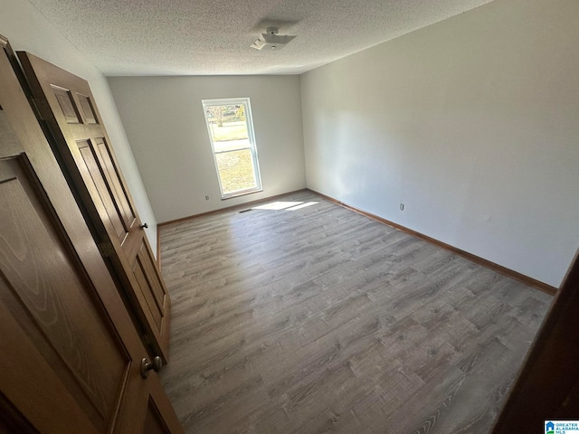 empty room with a textured ceiling and light hardwood / wood-style flooring