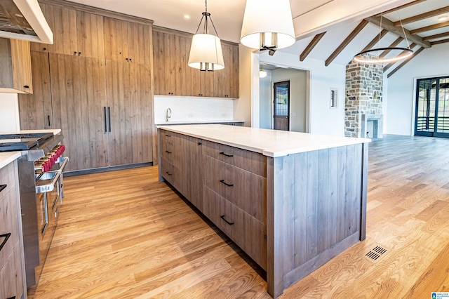 kitchen with a stone fireplace, light wood-type flooring, lofted ceiling with beams, and custom exhaust hood