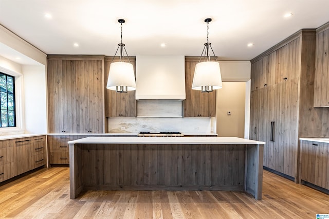 kitchen with a center island, decorative backsplash, hanging light fixtures, custom range hood, and light wood-type flooring