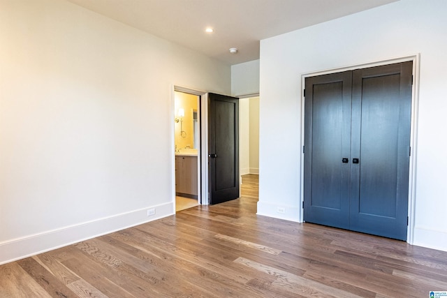 unfurnished bedroom with ensuite bathroom, hardwood / wood-style flooring, and a closet