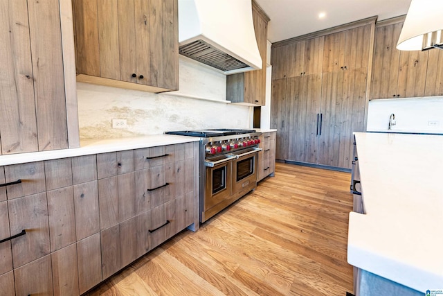 kitchen featuring range with two ovens, sink, backsplash, light wood-type flooring, and premium range hood