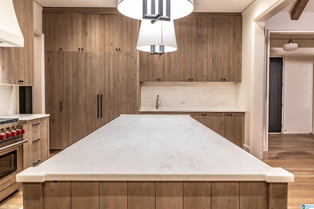 kitchen featuring a kitchen island, light wood-type flooring, hanging light fixtures, and premium range hood