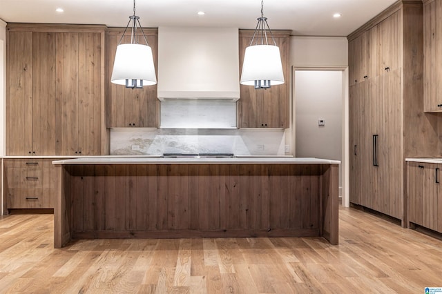 kitchen with light wood-type flooring, pendant lighting, custom range hood, and a center island