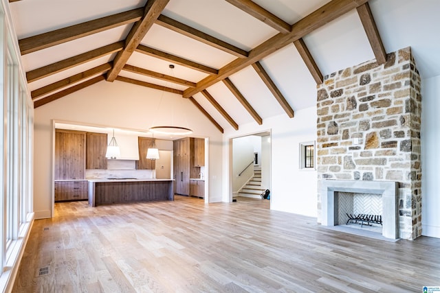 unfurnished living room with high vaulted ceiling, a fireplace, light hardwood / wood-style floors, and beam ceiling