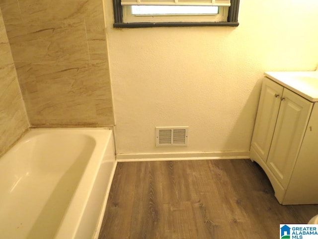 bathroom with hardwood / wood-style flooring, vanity, and a tub to relax in