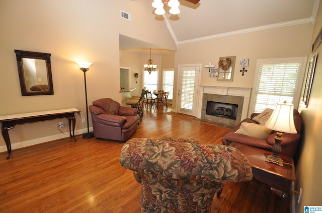 living room featuring hardwood / wood-style floors, a tiled fireplace, high vaulted ceiling, ornamental molding, and ceiling fan with notable chandelier