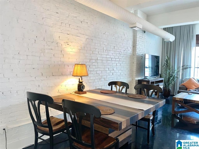 dining area with brick wall, a wealth of natural light, and concrete flooring