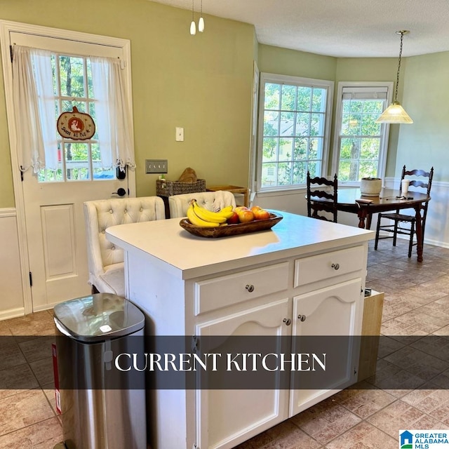 kitchen featuring a healthy amount of sunlight, decorative light fixtures, a kitchen island, and white cabinets