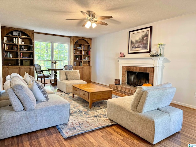 living room featuring ceiling fan, a textured ceiling, wood-type flooring, and a fireplace