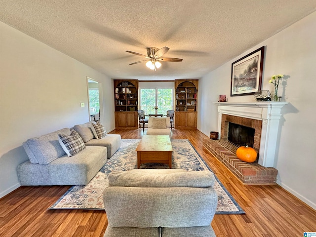 living room with a textured ceiling, ceiling fan, hardwood / wood-style floors, and a brick fireplace