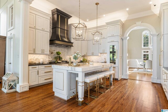 kitchen featuring premium range hood, dark hardwood / wood-style floors, hanging light fixtures, and decorative columns