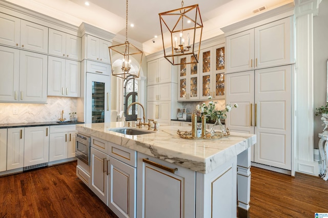 kitchen featuring hanging light fixtures, an island with sink, dark stone countertops, dark wood-type flooring, and sink