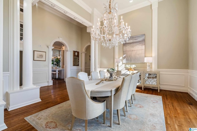 dining room with an inviting chandelier, wood-type flooring, decorative columns, ornamental molding, and a high ceiling