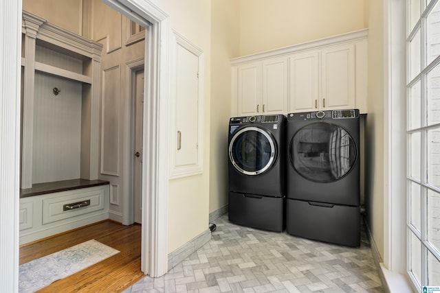 washroom with light hardwood / wood-style flooring, washing machine and clothes dryer, a healthy amount of sunlight, and cabinets