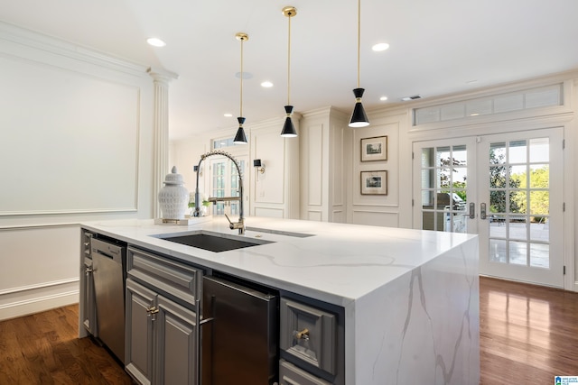 kitchen with sink, an island with sink, decorative light fixtures, dark wood-type flooring, and light stone counters