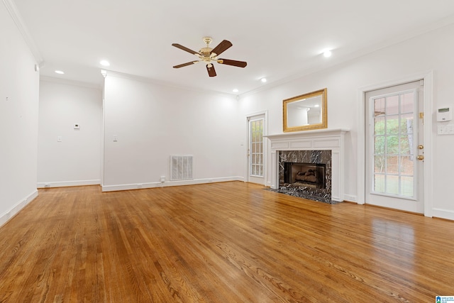 unfurnished living room with ornamental molding, a premium fireplace, wood-type flooring, and ceiling fan