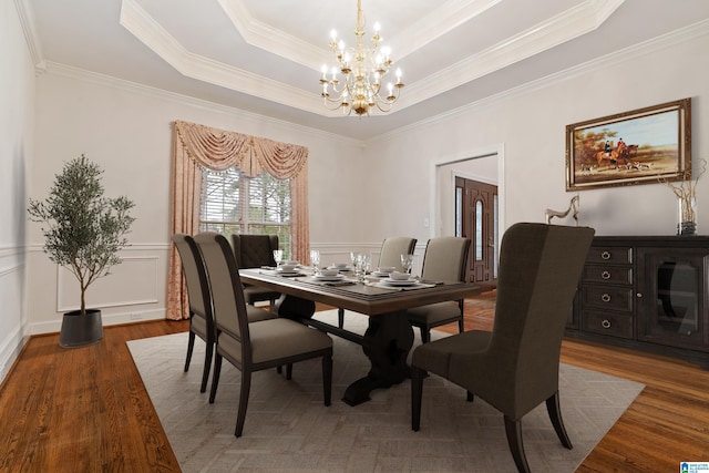 dining room with hardwood / wood-style flooring, a notable chandelier, a tray ceiling, and ornamental molding