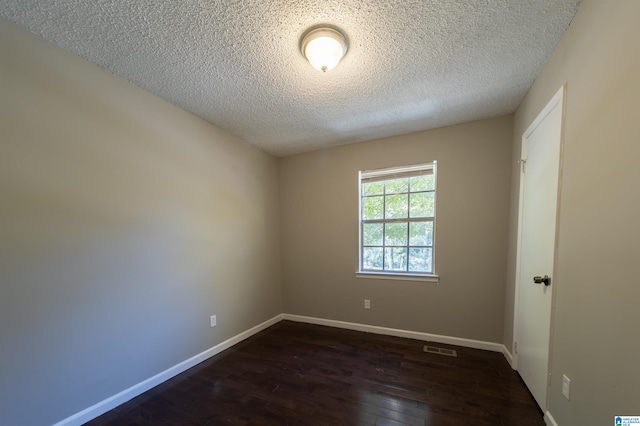 spare room with a textured ceiling and dark hardwood / wood-style flooring