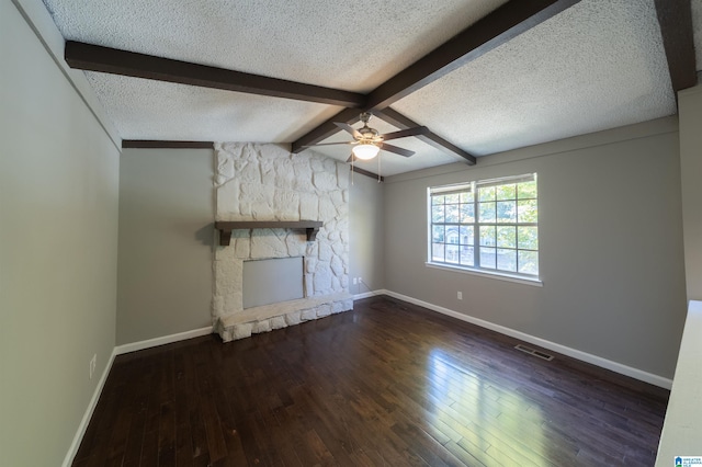 unfurnished living room with a stone fireplace, a textured ceiling, lofted ceiling with beams, and dark hardwood / wood-style floors