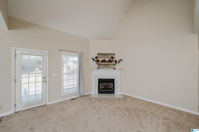 unfurnished living room featuring light carpet, high vaulted ceiling, and a premium fireplace