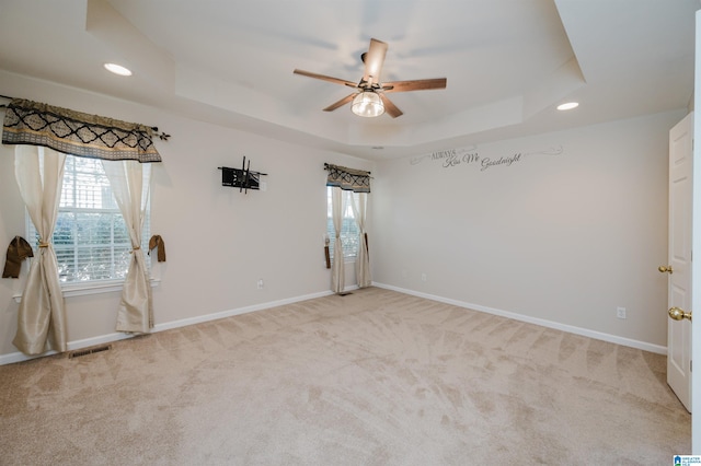 carpeted spare room featuring ceiling fan and a raised ceiling