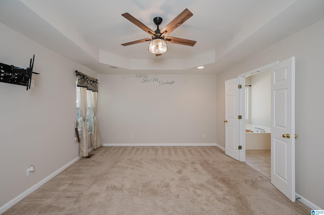 unfurnished bedroom with ceiling fan, a raised ceiling, and light colored carpet