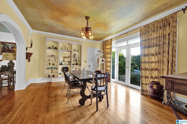 dining space with a notable chandelier, hardwood / wood-style flooring, built in features, crown molding, and french doors