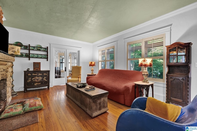 living room featuring french doors, crown molding, hardwood / wood-style flooring, and a stone fireplace