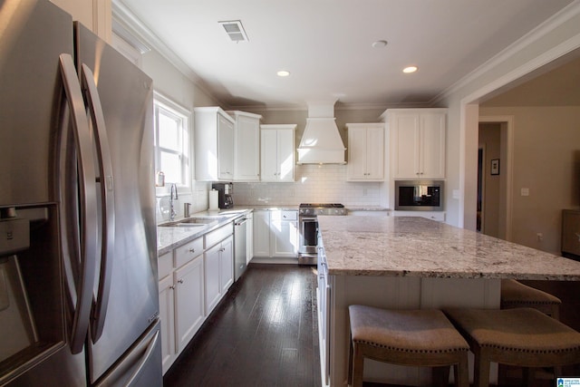 kitchen with light stone countertops, appliances with stainless steel finishes, a kitchen island, white cabinetry, and custom exhaust hood