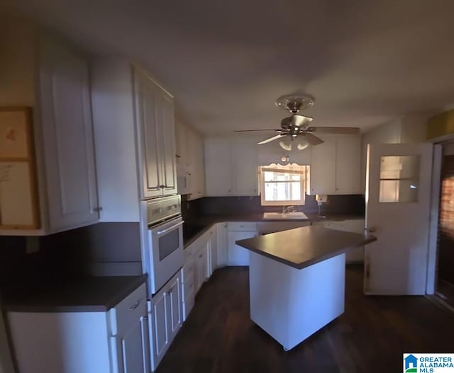 kitchen with white cabinets, ceiling fan, stainless steel oven, dark wood-type flooring, and sink