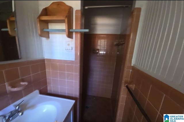 bathroom with a tile shower, vanity, and tile walls