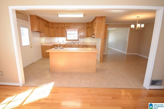 kitchen with a kitchen island, a sink, light countertops, baseboards, and light tile patterned flooring
