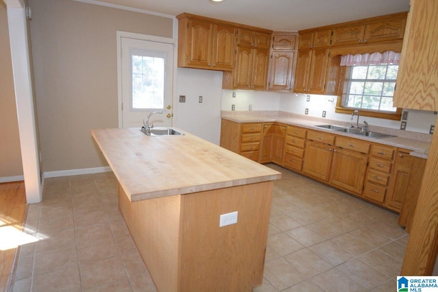 kitchen with butcher block countertops, a sink, light tile patterned floors, and a center island with sink