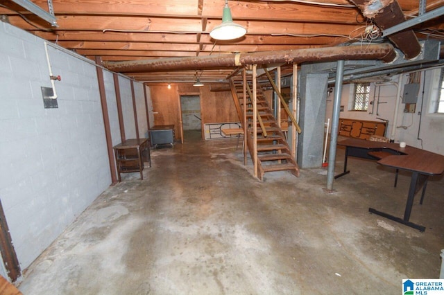 basement with concrete block wall, stairway, and electric panel