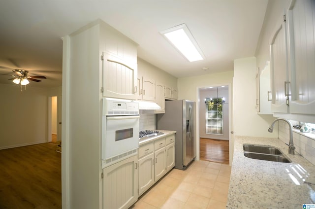 kitchen featuring sink, white cabinetry, stainless steel appliances, light stone counters, and decorative backsplash