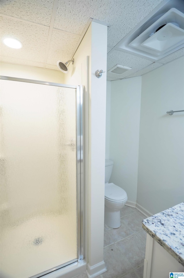 bathroom with a paneled ceiling, a shower with shower door, vanity, toilet, and tile patterned floors