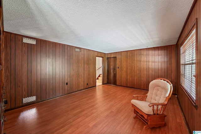 unfurnished room with wood walls, a textured ceiling, and light hardwood / wood-style flooring