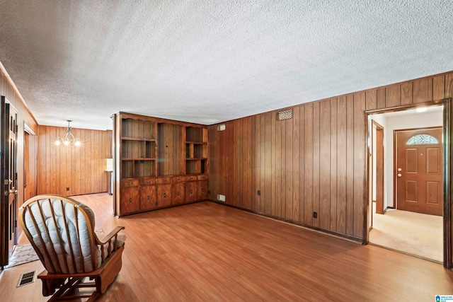 living area featuring a textured ceiling, hardwood / wood-style flooring, a chandelier, and wooden walls