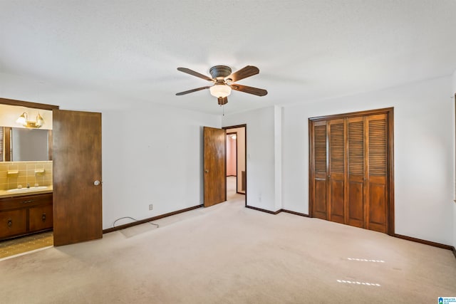 unfurnished bedroom featuring a closet, ensuite bath, sink, light colored carpet, and ceiling fan