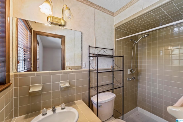 bathroom with toilet, sink, tile walls, and tiled shower