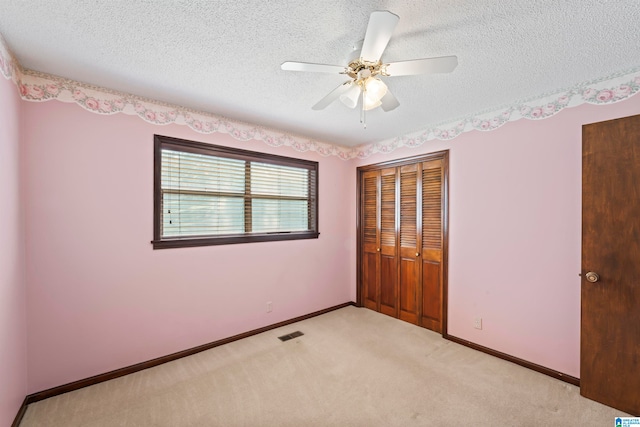 unfurnished bedroom featuring light carpet, a closet, a textured ceiling, and ceiling fan