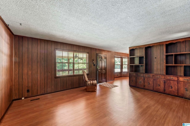 unfurnished living room featuring a textured ceiling, wooden walls, wood-type flooring, and plenty of natural light