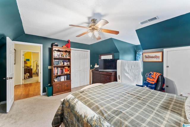 bedroom with a textured ceiling, a closet, ceiling fan, vaulted ceiling, and light colored carpet