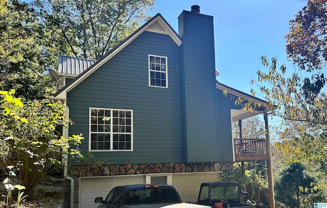 view of side of property featuring a chimney, an attached garage, and a balcony