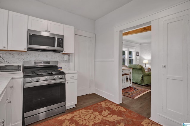 kitchen with dark wood-type flooring, light countertops, white cabinetry, tasteful backsplash, and stainless steel appliances